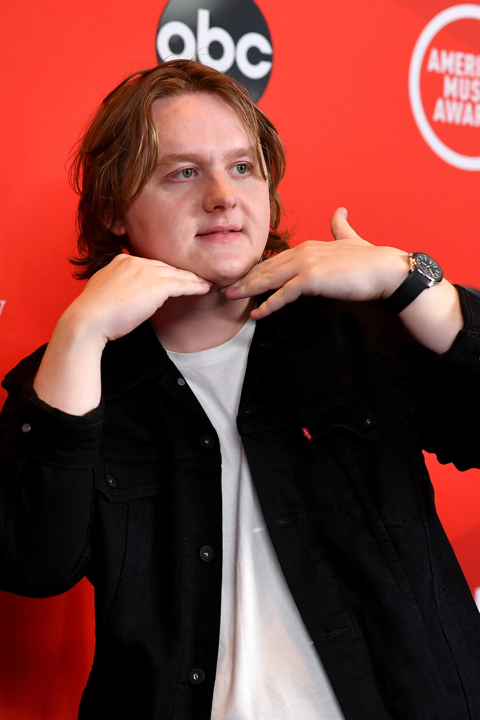 Lewis Capaldi posing on a red carpet wearing a black shirt over a white t shirt