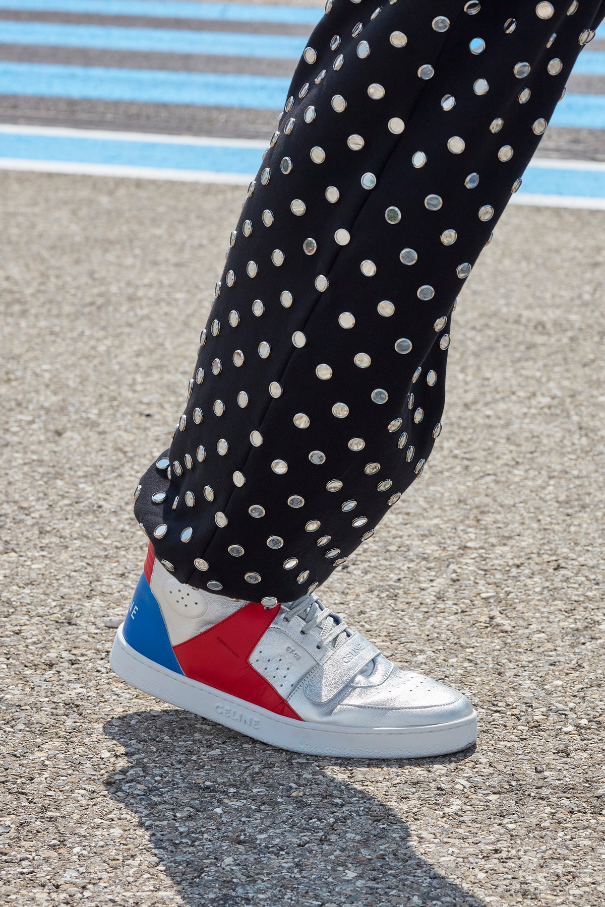 A close up of a model wearing polka dot pants and red white and blue celine sneakers