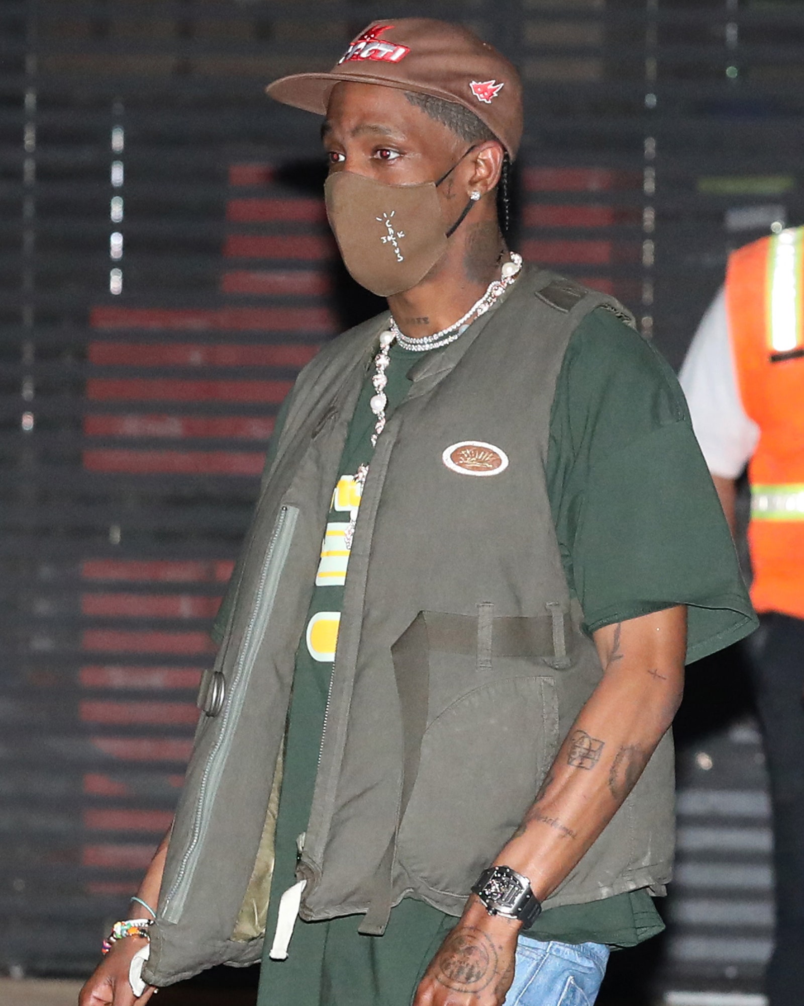 Travis Scott walking on the street wearing a vest and long green teeshirt