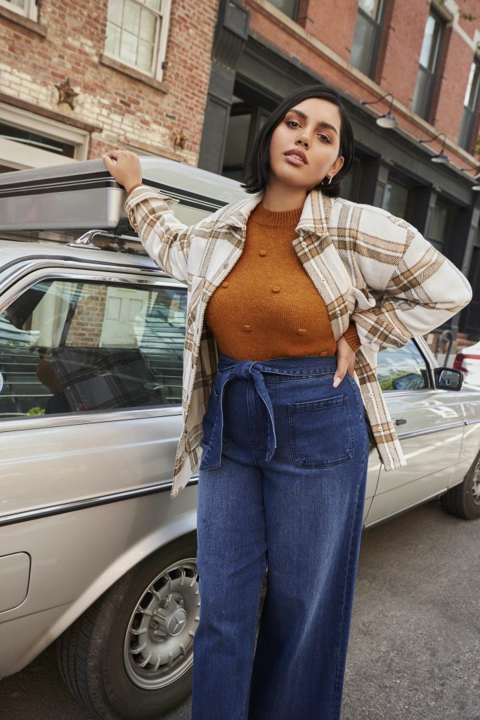 Woman standing against car in sweater, jacket and jeans from ELOQUII elements.