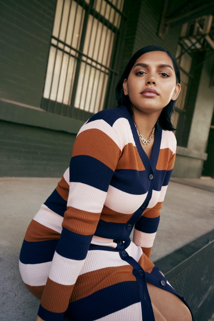 Woman sitting wearing ELOQUII elements striped sweater dress.